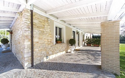 Porticato in abete lamellare e perlinato sbiancati. Pavimentazione con cubetti di porfido, rivestimento con Kerma Biopietra